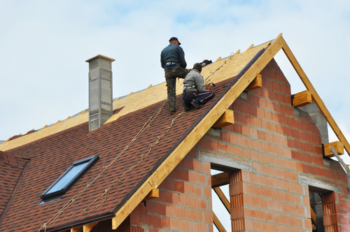 two men on roof, replacing shingles.