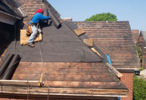 man tied up to roof for safety, repairing and replacing roofing.