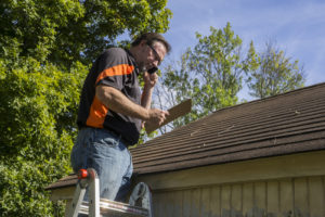 Contractor on ladder with cell phone figuring out hail damage repair costs for customer.